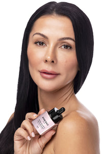 woman holding pink serum bottle that says knesko skin rose quartz antioxidant serum.